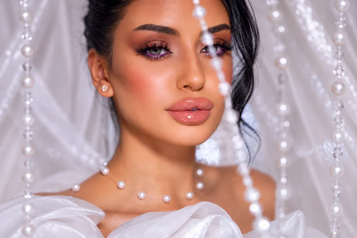 Violet eyeliner and glossy lips behind delicate pearl strands