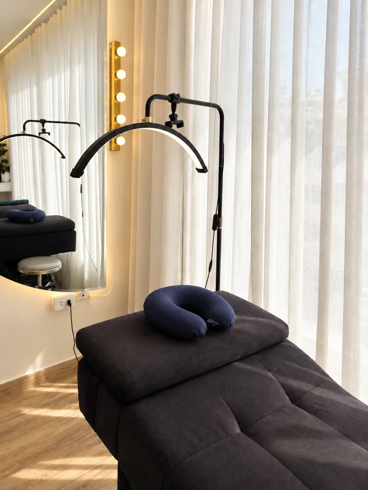 A dark beauty chair with a curved task light beside sheer window curtains